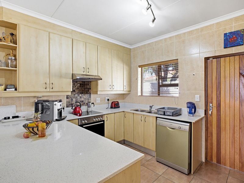 Functional kitchen featuring light wood cabinetry, stone countertops, tiled backsplash, and integrated appliances, offering a practical layout with direct access to an exterior door.