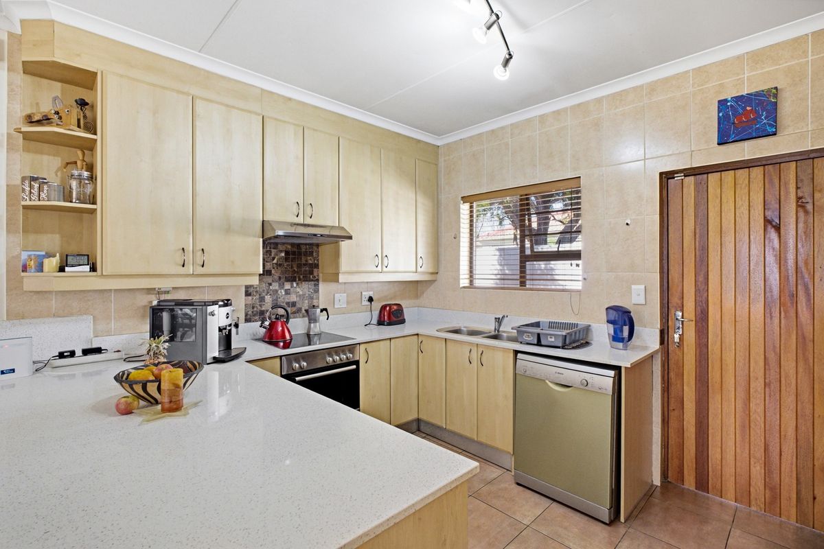 Functional kitchen featuring light wood cabinetry, stone countertops, tiled backsplash, and integrated appliances, offering a practical layout with direct access to an exterior door.