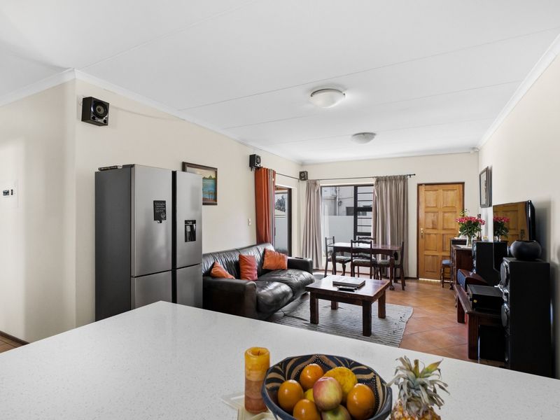 Open-plan living and dining area featuring tiled flooring, a modern quartz kitchen island, and direct access to the exterior through a timber door.