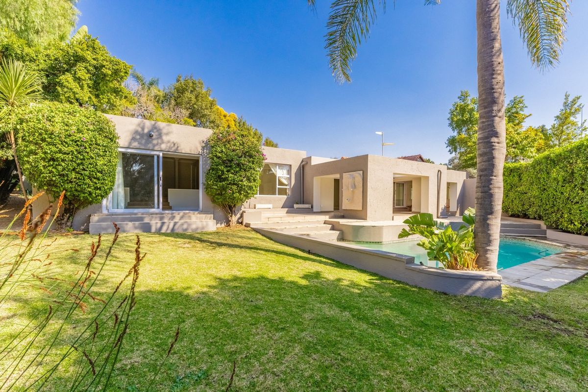 Rear exterior view of the property featuring a swimming pool, concrete patio area, and well-maintained garden with mature landscaping.