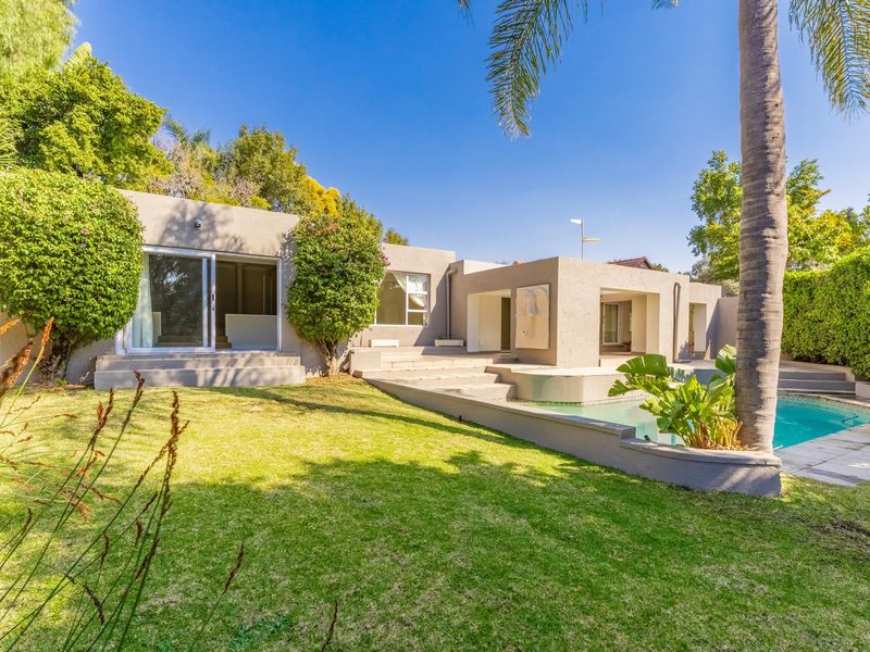 Rear exterior view of the property featuring a swimming pool, concrete patio area, and well-maintained garden with mature landscaping.
