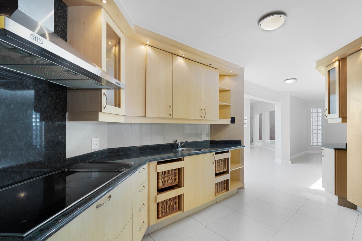 Modern kitchen featuring light wood cabinetry, dark granite countertops, integrated hob, extractor fan, and tiled flooring, leading into an open-plan living area.