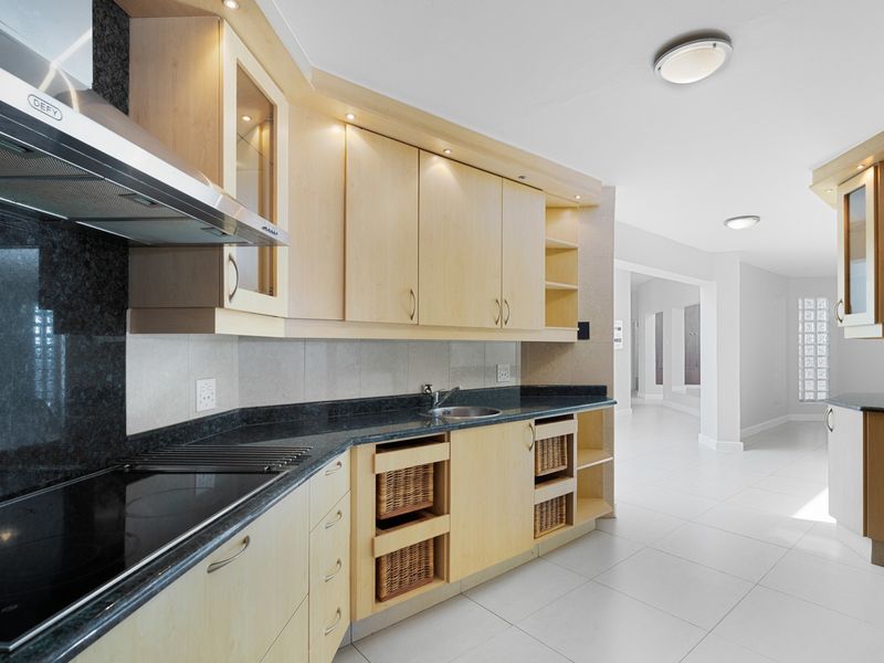 Modern kitchen featuring light wood cabinetry, dark granite countertops, integrated hob, extractor fan, and tiled flooring, leading into an open-plan living area.