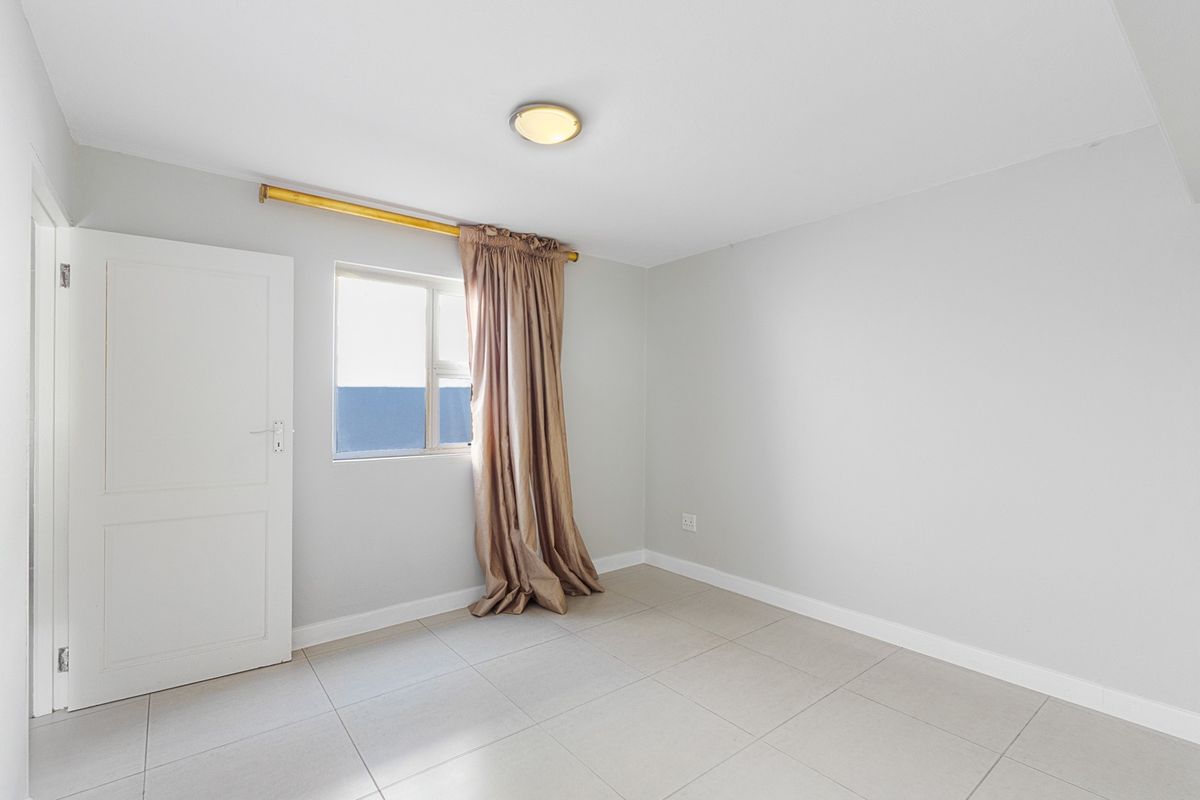 A clean, empty bedroom featuring neutral tiled flooring, a flush mount ceiling light, and a window with a curtain rod.