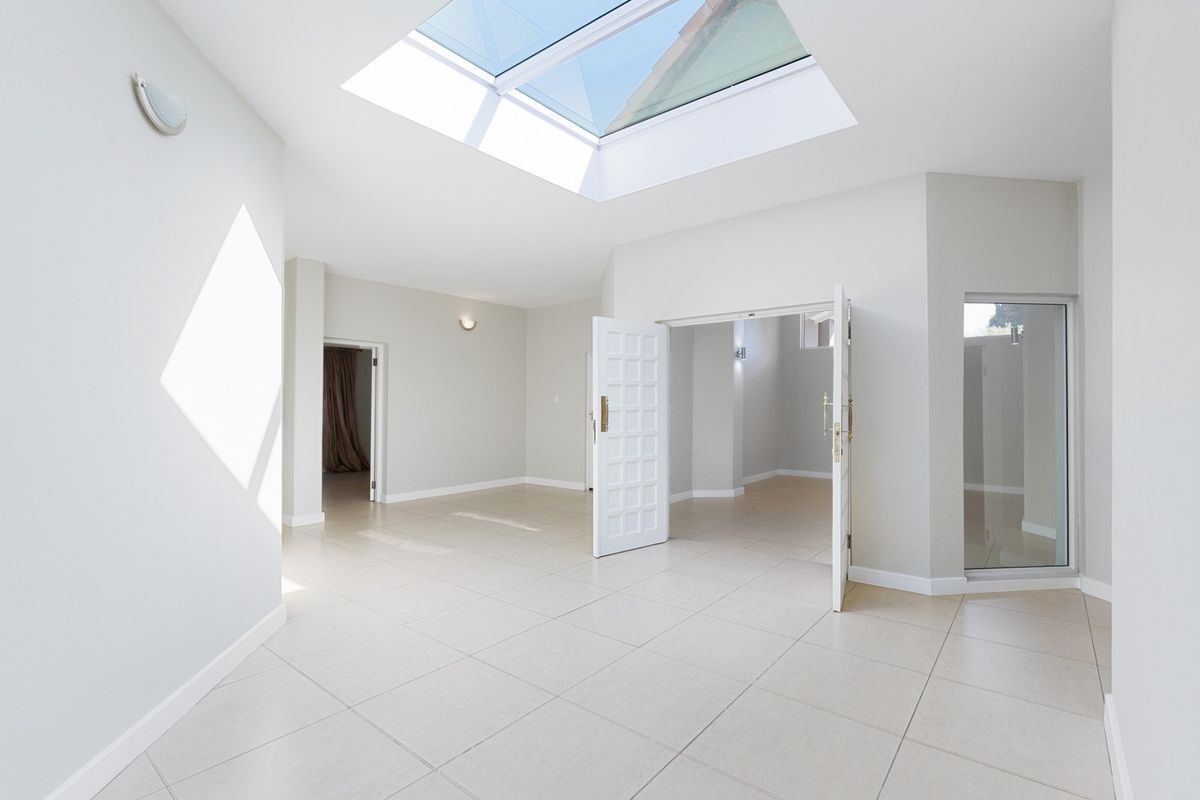 A bright and spacious living area featuring large format floor tiles, a prominent skylight, and double door access to adjacent rooms.