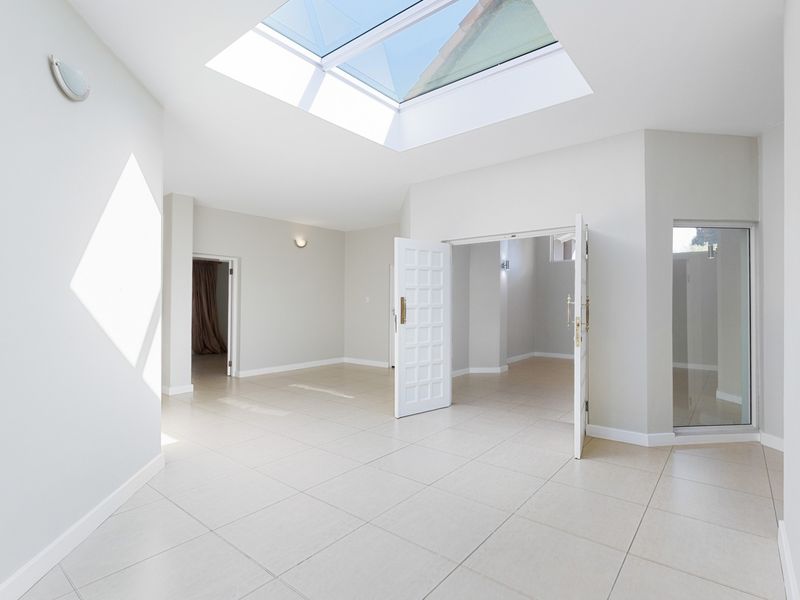 A bright and spacious living area featuring large format floor tiles, a prominent skylight, and double door access to adjacent rooms.