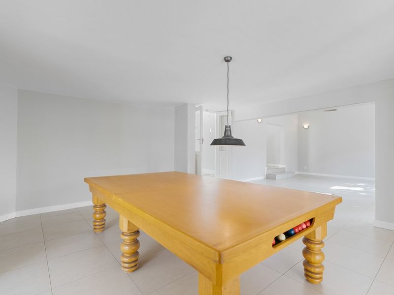 Spacious living area featuring neutral tiled flooring and a modern pendant light fixture, offering a versatile space for recreation or relaxation.