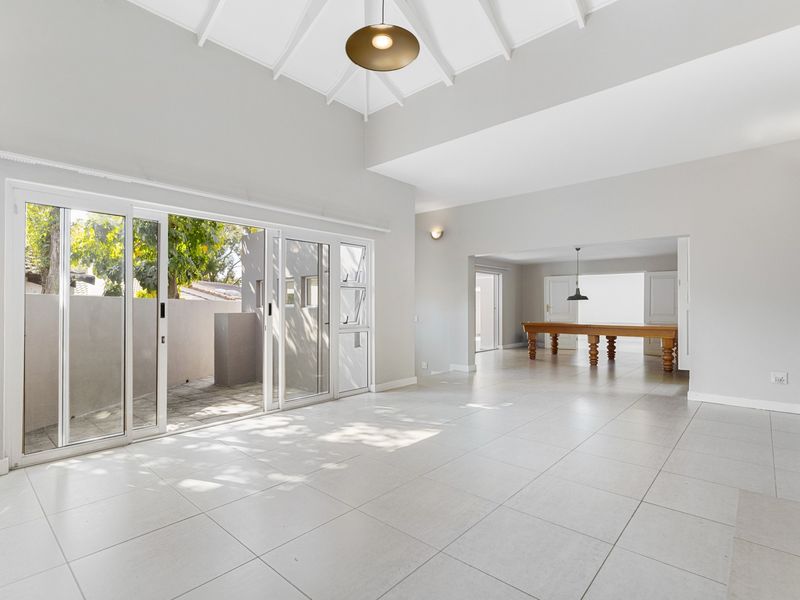 Spacious open-plan living area featuring vaulted ceilings, neutral tiled flooring, and large sliding glass doors providing seamless access to the outdoor patio.