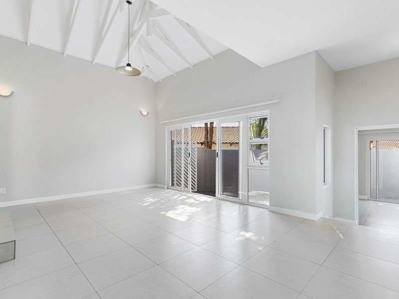 Spacious living area featuring high vaulted ceilings with exposed rafters, neutral tiled flooring, and large sliding glass doors providing access to the exterior.
