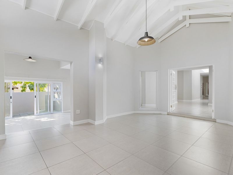 Spacious living area featuring high vaulted ceilings with exposed rafters, neutral tiled flooring, and abundant natural light through large sliding glass doors.