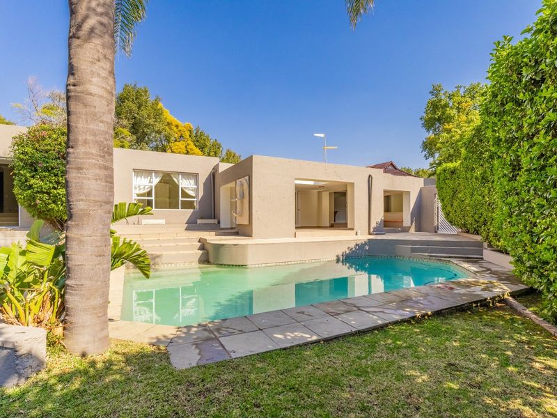 Rear exterior view featuring a swimming pool, paved pool deck, and a covered patio area set within a landscaped garden.