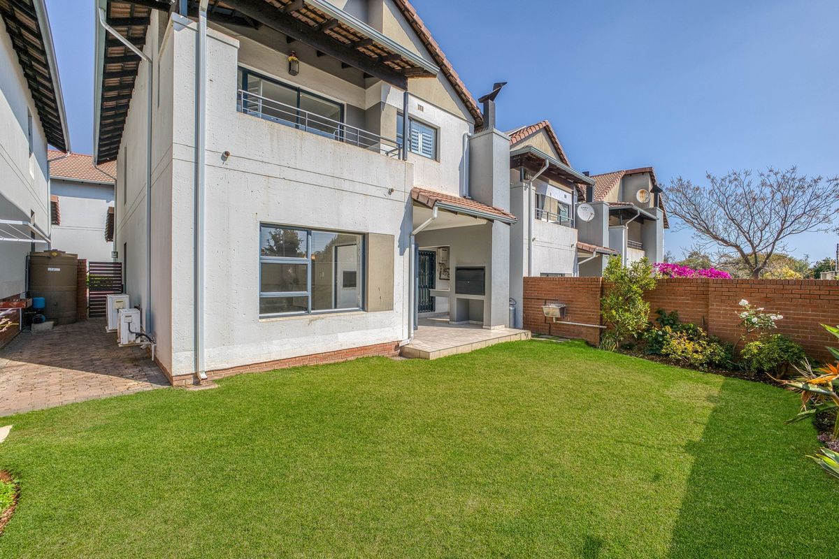 Rear view of the townhouse featuring a private garden, paved patio with built-in braai, and an upper-level balcony.