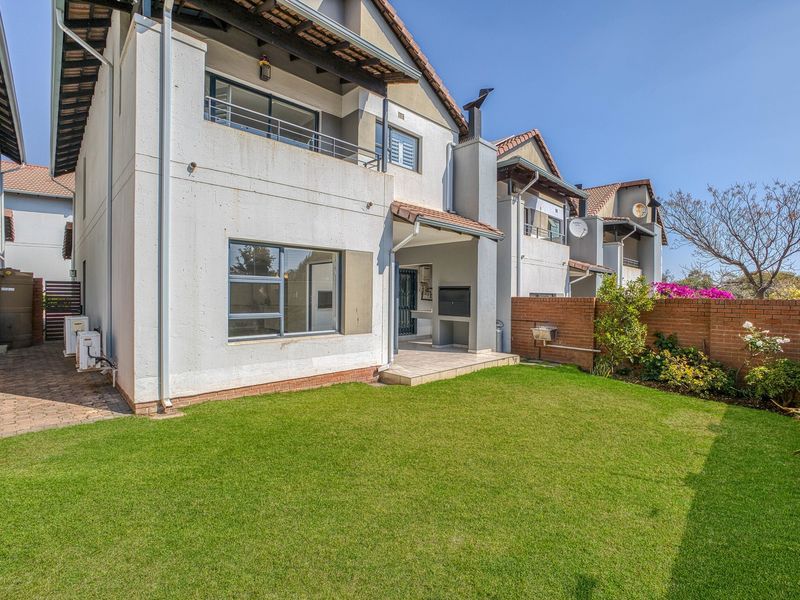 Rear view of the townhouse featuring a private garden, paved patio with built-in braai, and an upper-level balcony.