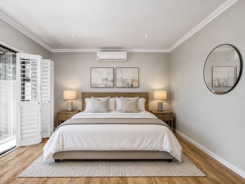 A well-maintained bedroom featuring laminate flooring, crown molding, recessed lighting, an air conditioning unit, and sliding glass doors with plantation shutters.