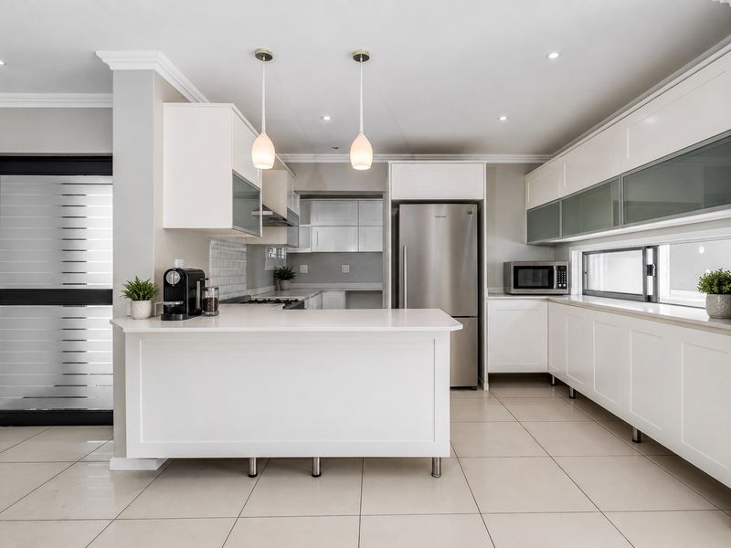 Modern kitchen featuring white cabinetry, stone countertops, subway tile backsplash, stainless steel appliances, and tiled flooring with ample storage and workspace.
