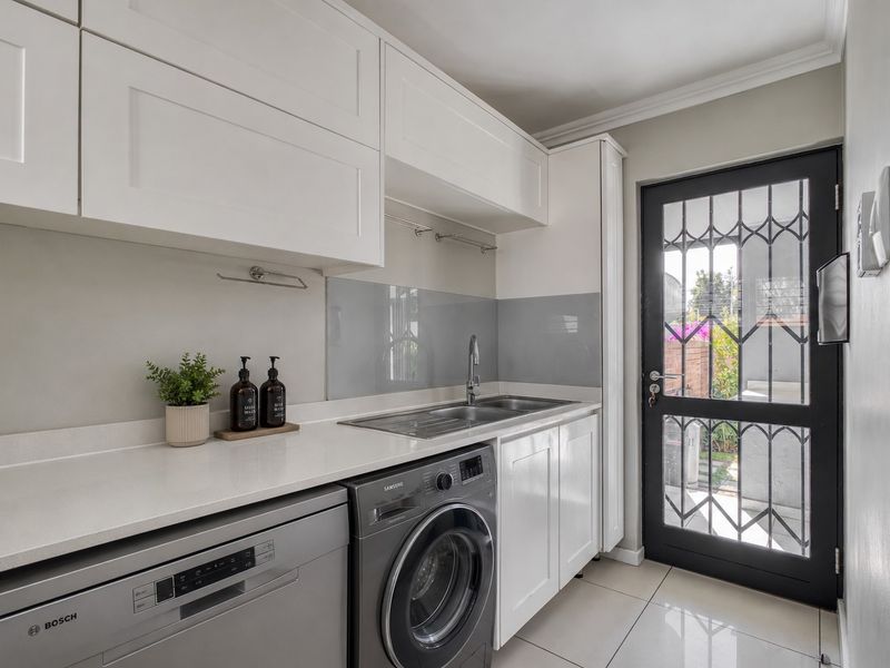 Modern scullery featuring white cabinetry, stone countertops, stainless steel sink, and direct access to the exterior via a secure door.