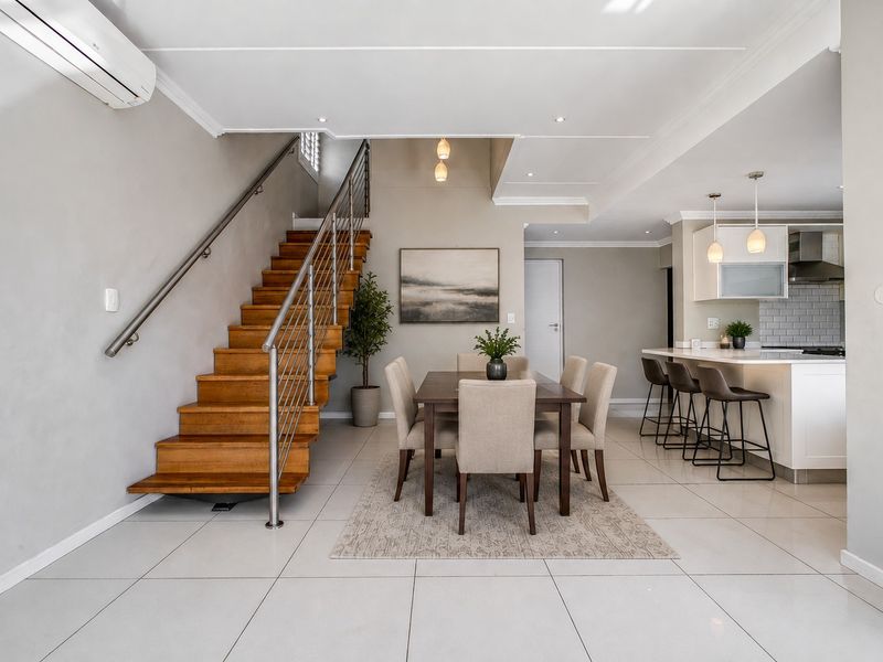 Modern open-plan living area featuring a timber staircase with stainless steel balustrade, tiled flooring, and a contemporary kitchen with island and subway tile backsplash.