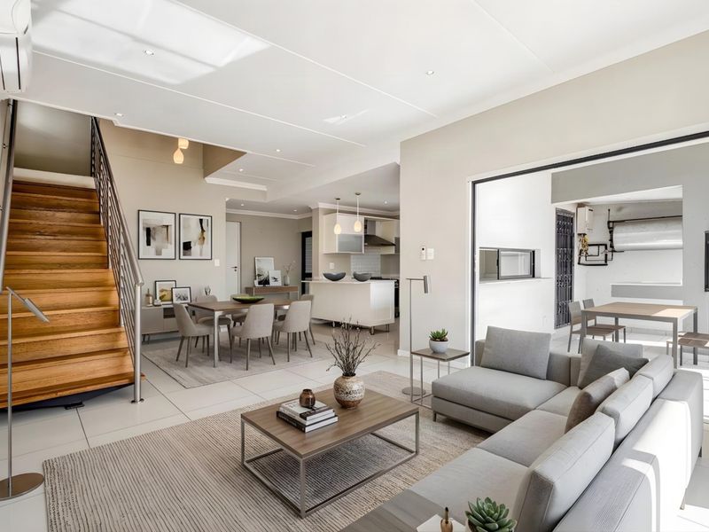 Spacious open-plan living and dining area featuring a timber staircase, modern kitchen island, and seamless flow to the outdoor patio through stacking doors.
