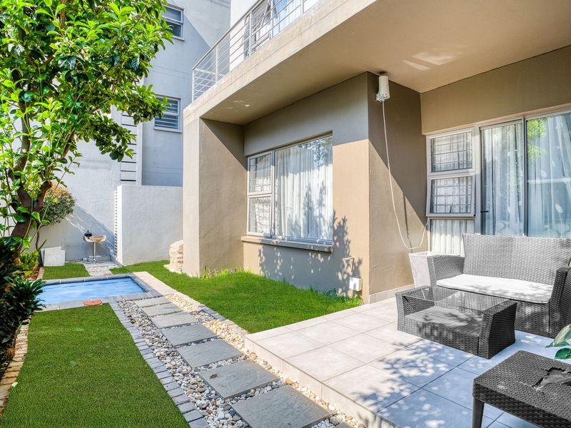 Rear exterior view featuring a tiled patio, small plunge pool, stone walkway, and artificial lawn area with access via sliding glass doors.
