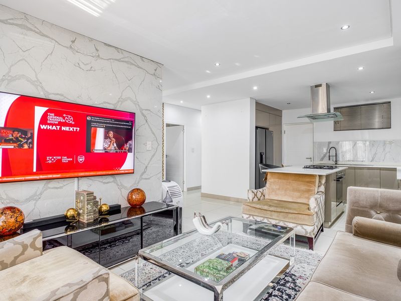 Modern open-plan living area featuring a marble-look feature wall, sleek kitchen with island, gas hob, and integrated appliances, finished with high-quality tiling.