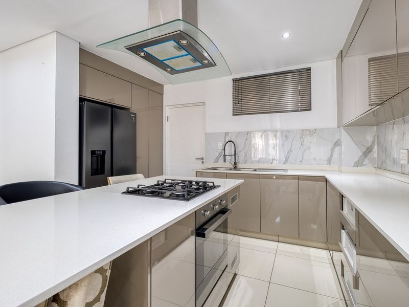 Modern kitchen featuring high-gloss cabinetry, stone countertops, a central island with a gas hob, and premium marble-look splashbacks.
