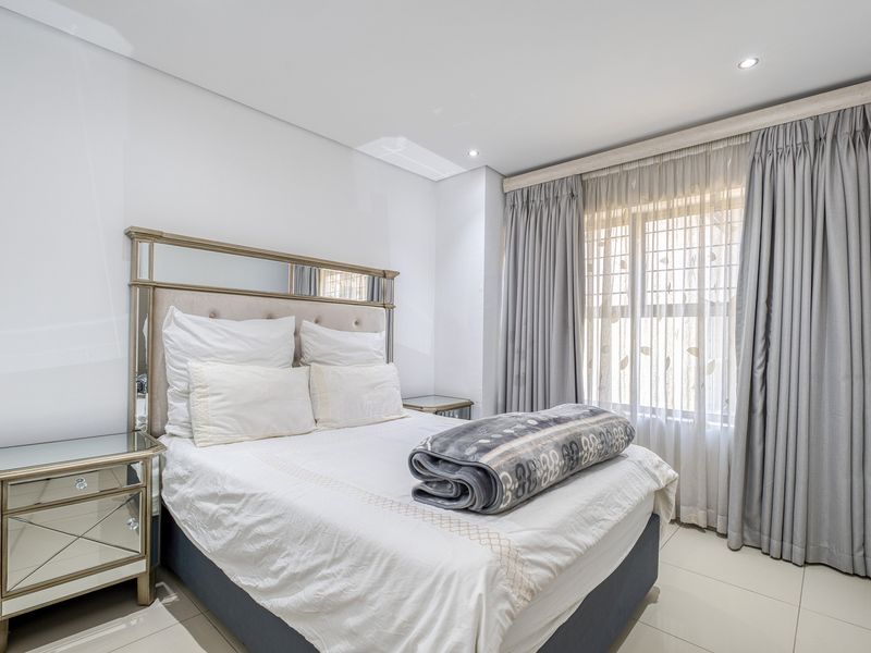 A well-maintained bedroom featuring neutral tiled flooring, recessed downlighting, and floor-to-ceiling curtain tracks, offering a clean and bright living space.