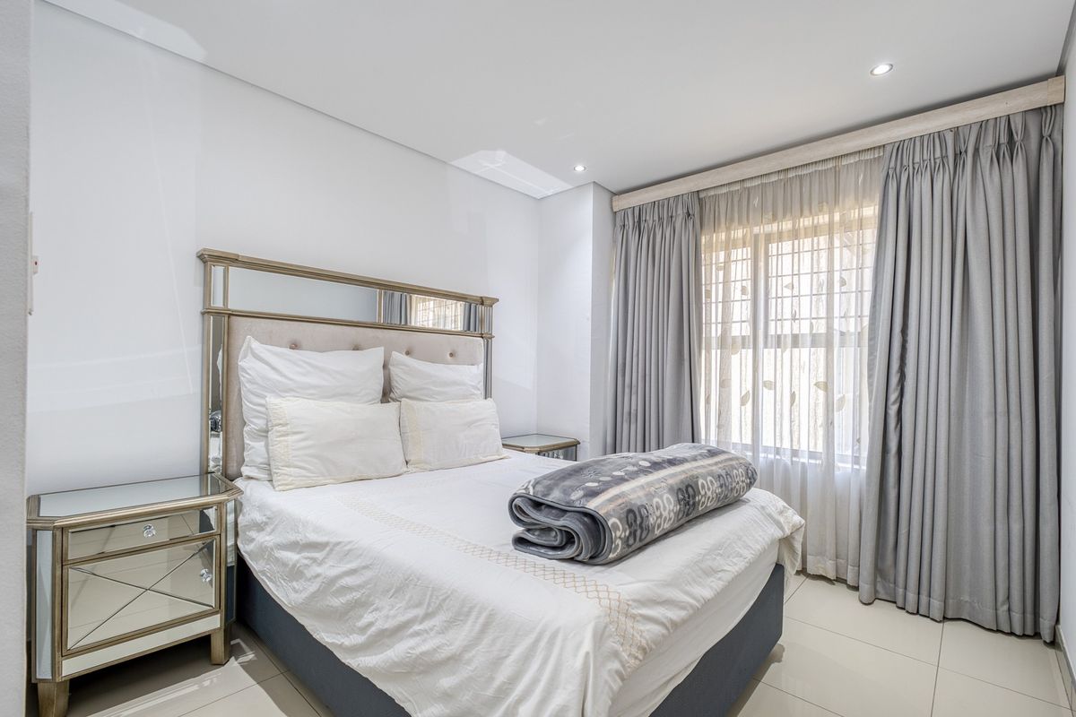A well-maintained bedroom featuring neutral tiled flooring, recessed downlighting, and floor-to-ceiling curtain tracks, offering a clean and bright living space.