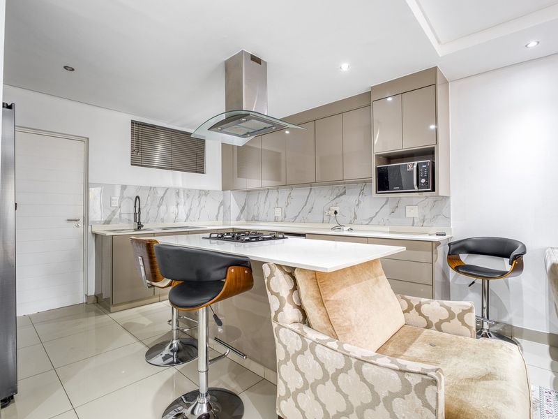 Modern kitchen featuring high-gloss cabinetry, stone countertops, a gas hob with extractor fan, and a stylish marble-look splashback.