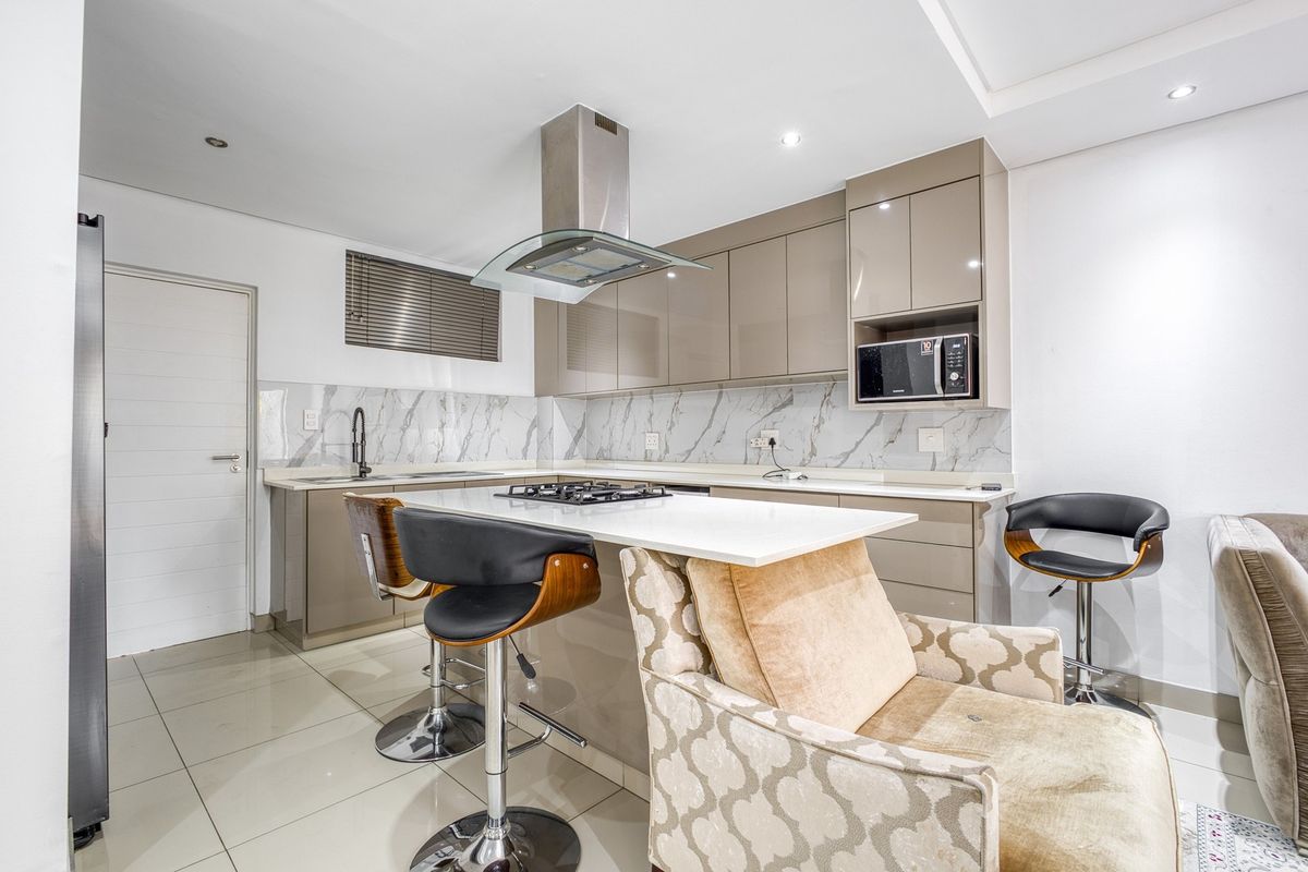 Modern kitchen featuring high-gloss cabinetry, stone countertops, a gas hob with extractor fan, and a stylish marble-look splashback.