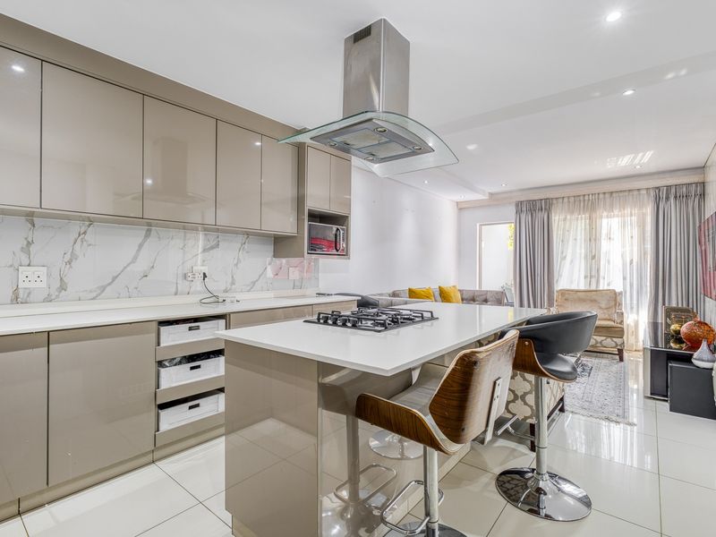Modern open-plan kitchen and living area featuring high-gloss cabinetry, stone countertops, a gas hob, and sleek porcelain floor tiles throughout.