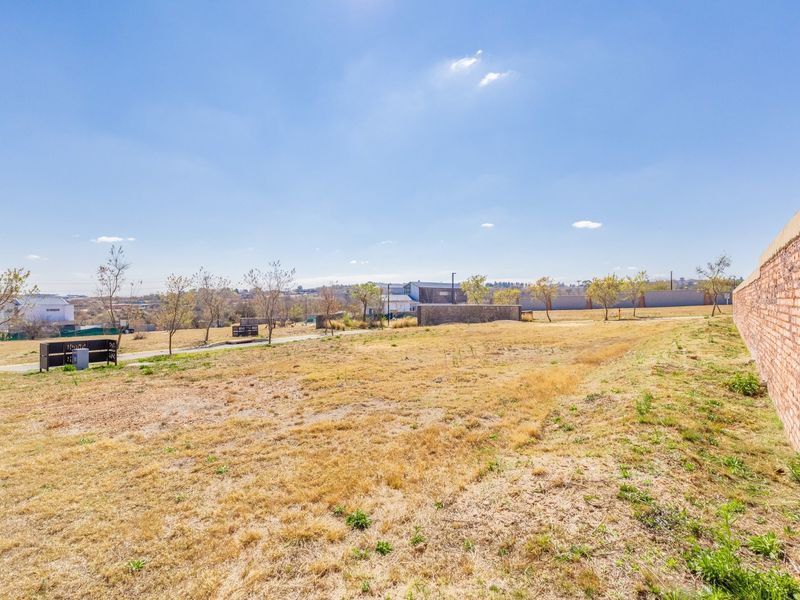 A view of a vacant residential plot featuring a brick boundary wall and open grassed area.