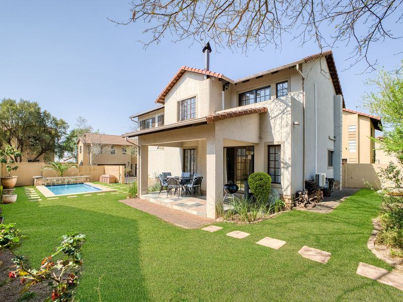 Rear view of the property featuring a covered patio, landscaped garden, and a private swimming pool with paved surrounds.