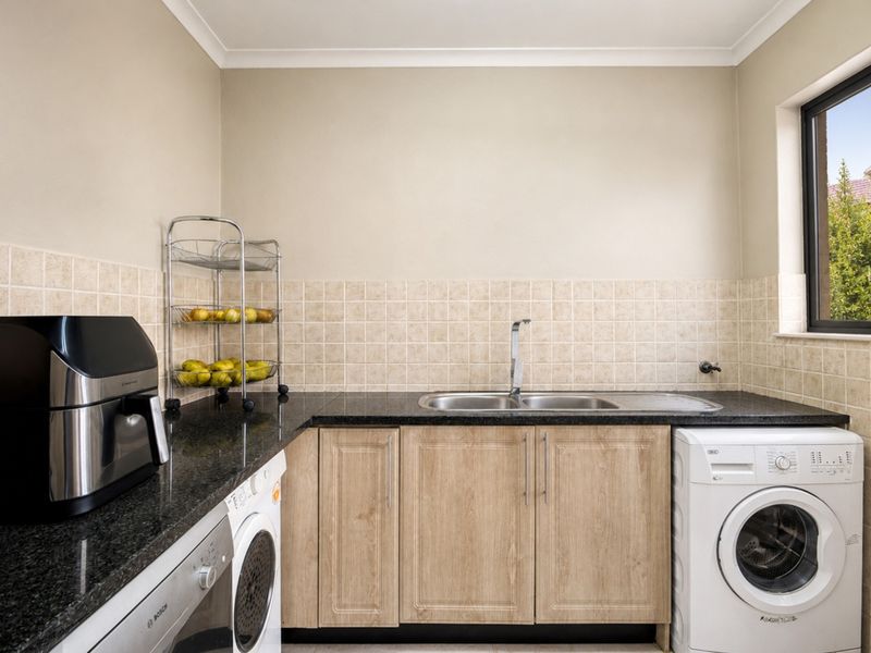 A functional laundry room featuring granite countertops, a double basin sink, tiled backsplash, and built-in cabinetry with dedicated appliance connections.
