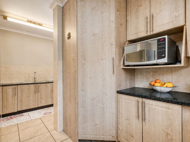A functional scullery area featuring light wood-finish cabinetry, granite countertops, a stainless steel sink, and a built-in microwave space.
