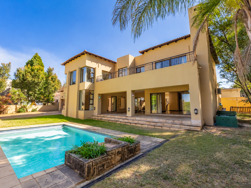 Rear view of a two-story house featuring a swimming pool, tiled patio, upper-level balcony, and large sliding glass doors opening to the interior.