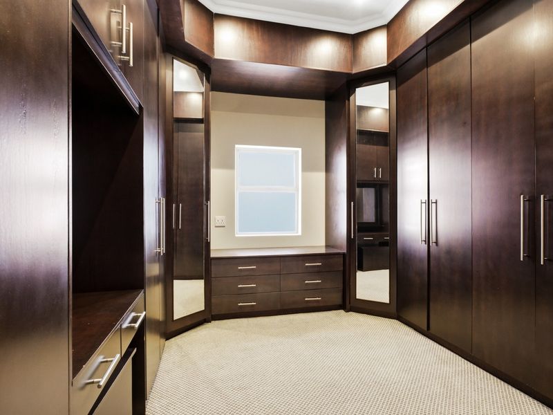 A spacious walk-in dressing room featuring extensive dark wood built-in cabinetry, integrated mirrored wardrobe doors, and ample drawer storage.