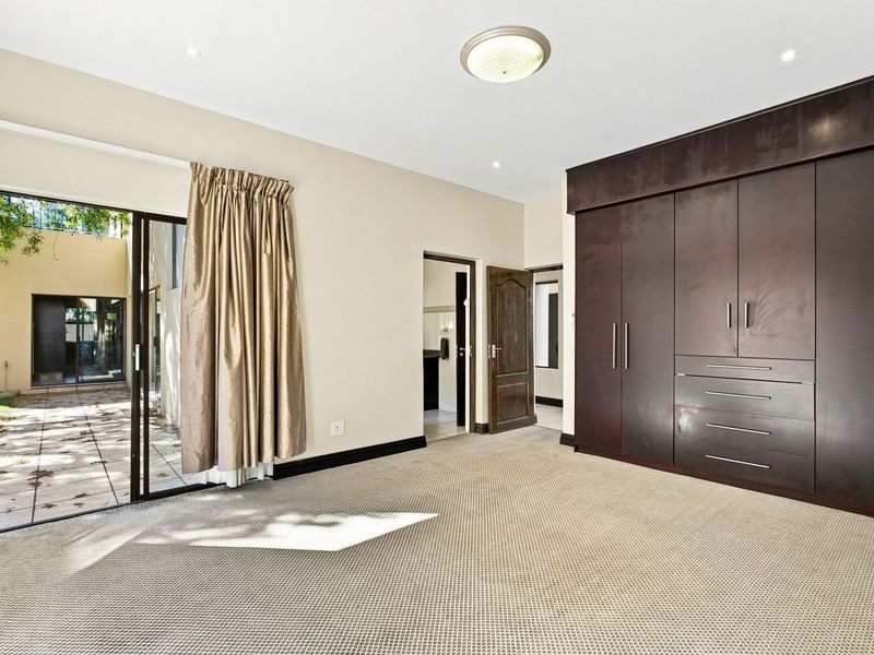 Spacious bedroom featuring built-in dark wood cupboards, neutral carpeting, and a sliding glass door providing direct access to an outdoor patio area.