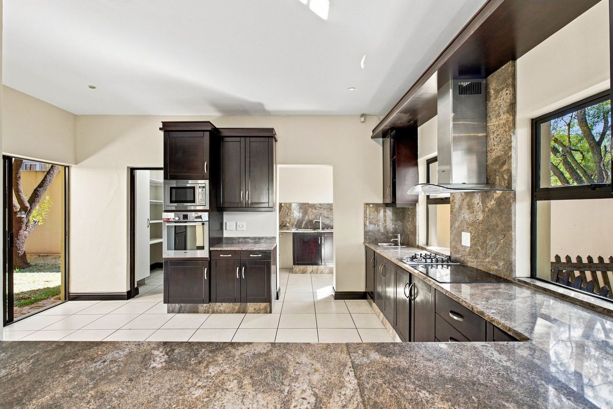 Modern kitchen featuring dark wood cabinetry, granite countertops, built-in appliances, and a gas hob, with direct access to a scullery and outdoor area.