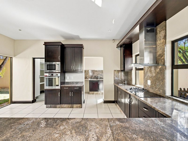 Modern kitchen featuring dark wood cabinetry, granite countertops, built-in appliances, and a gas hob, with direct access to a scullery and outdoor area.