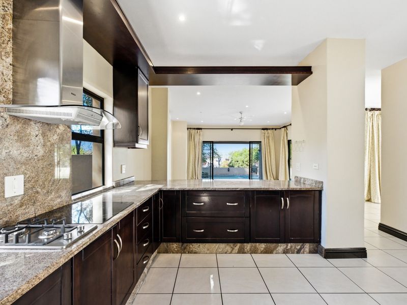 Modern kitchen featuring dark wood cabinetry, granite countertops, and a gas hob, with an open-plan layout flowing into the living area.