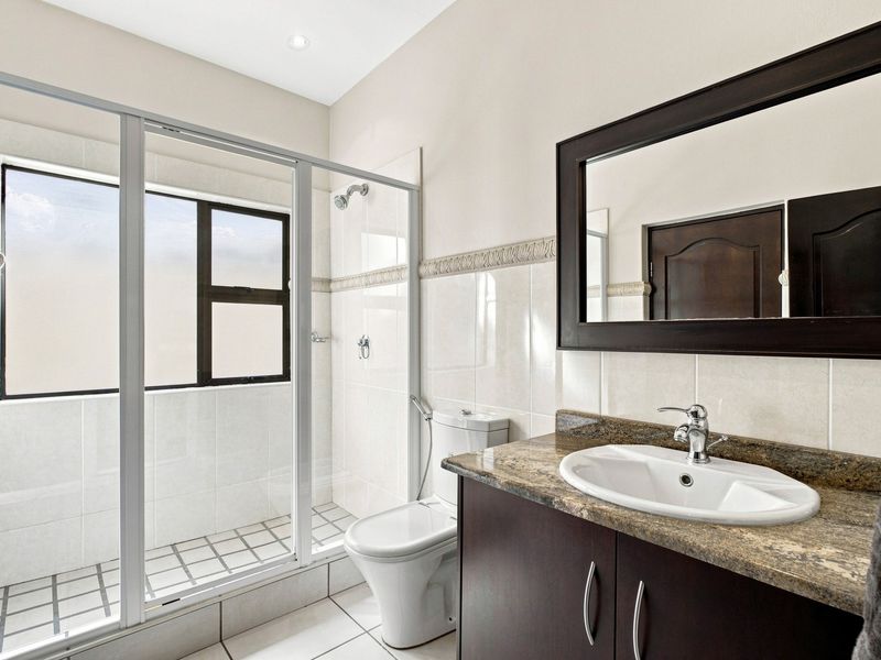 A clean, functional bathroom featuring a glass-enclosed shower, a dark wood vanity with a granite countertop, and neutral wall tiling.