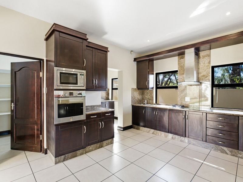 Spacious kitchen featuring dark wood cabinetry, stone countertops, built-in appliances, and an adjacent walk-in pantry with tiled flooring throughout.