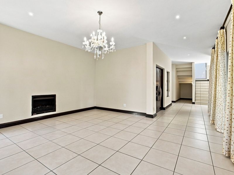 Spacious living area featuring neutral tiled flooring, a built-in fireplace, recessed lighting, and an adjacent staircase leading to the upper level.