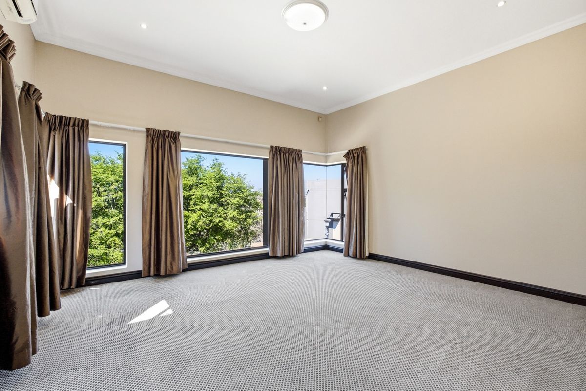 Spacious, light-filled bedroom featuring large corner windows, neutral wall tones, carpeted flooring, and an integrated air conditioning unit.