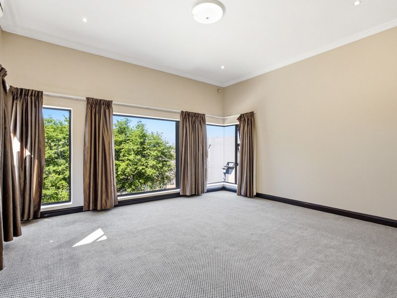 Spacious, light-filled bedroom featuring large corner windows, neutral wall tones, carpeted flooring, and an integrated air conditioning unit.