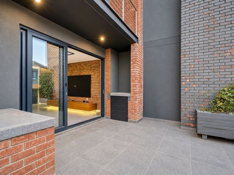 A modern covered balcony featuring tiled flooring, brick masonry accents, and a large sliding glass door providing seamless access to the interior living space.