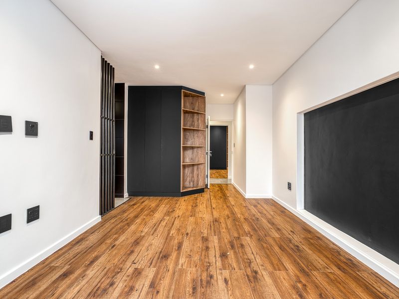 A modern, well-lit hallway featuring high-quality laminate flooring, sleek built-in cabinetry, and a contemporary black feature wall.