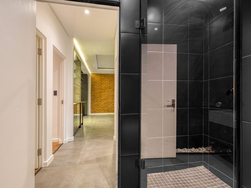 Modern bathroom featuring a sleek walk-in shower with black tiling and glass enclosure, leading into a well-lit hallway with contemporary finishes.