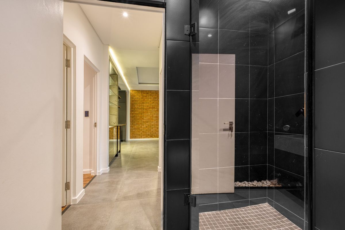 Modern bathroom featuring a sleek walk-in shower with black tiling and glass enclosure, leading into a well-lit hallway with contemporary finishes.
