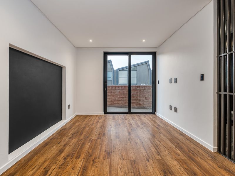 A bright, modern, and empty living area featuring wood-look laminate flooring, recessed lighting, and a sliding glass door leading to an outdoor space.